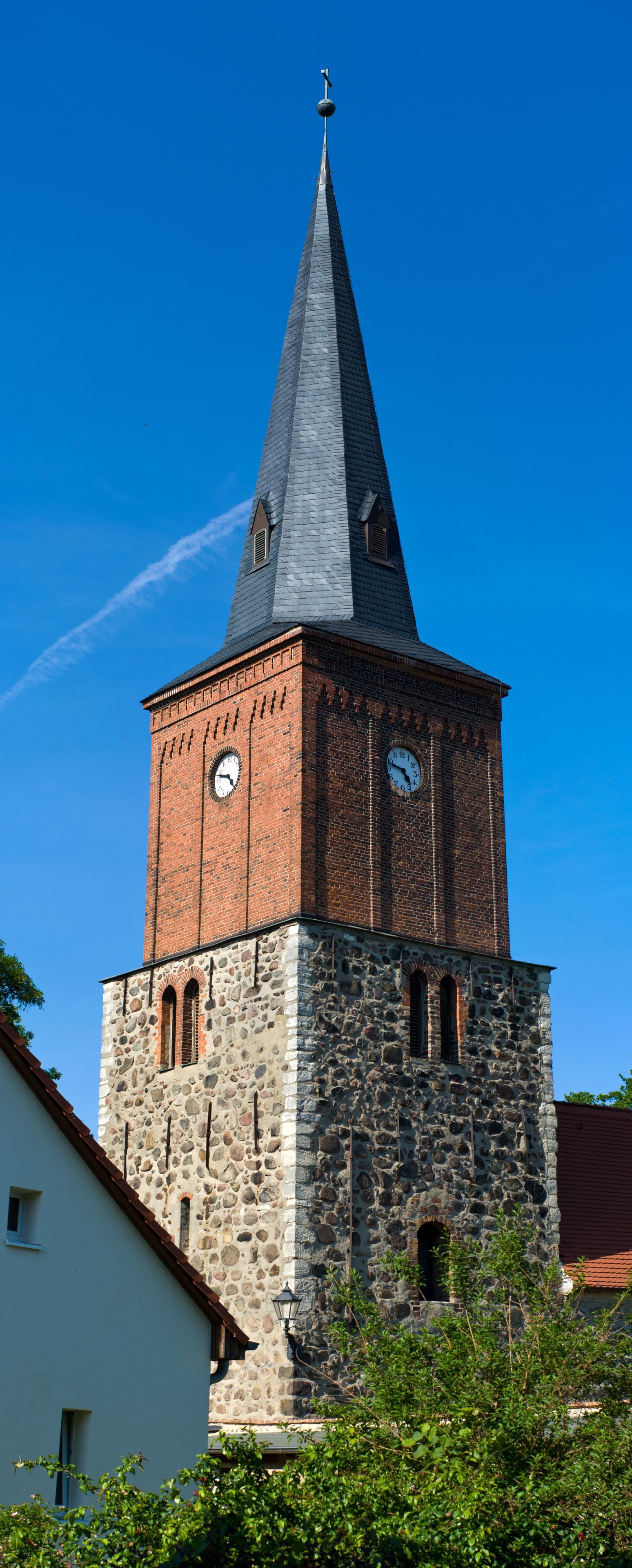 A church tower with a clock, a pointed spire, and a clear blue sky.