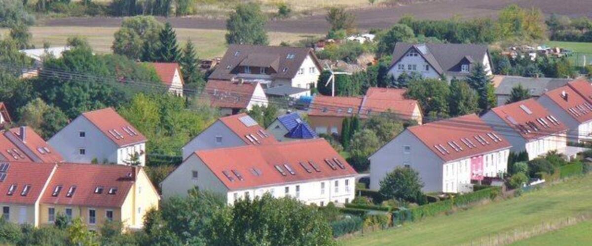 A lakeside village with red-roofed houses, a large body of water, and surrounding greenery.