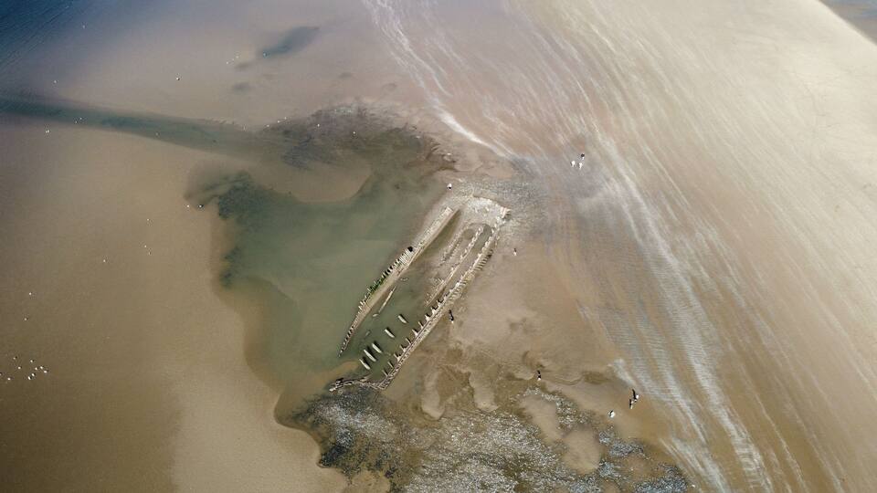 A sandy beach with a partially submerged structure, possibly a shipwreck, and a clear demarcation of water and sand.