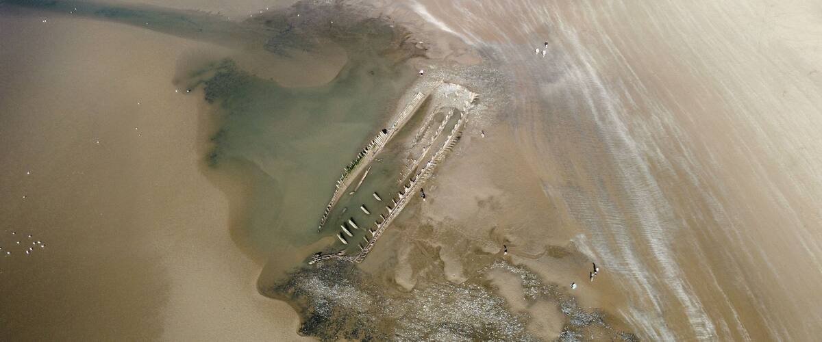 A sandy beach with a partially submerged structure, possibly a shipwreck, and a clear demarcation of water and sand.