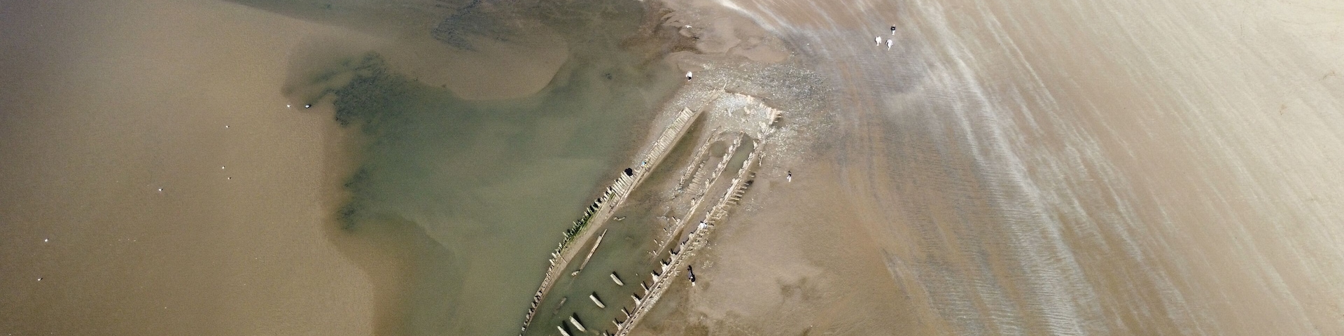 A sandy beach with a partially submerged structure, possibly a shipwreck, and a clear demarcation of water and sand.