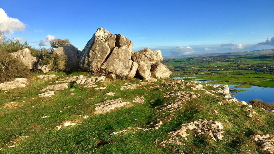 A rocky landscape with a large boulder formation and a lake in the distance.