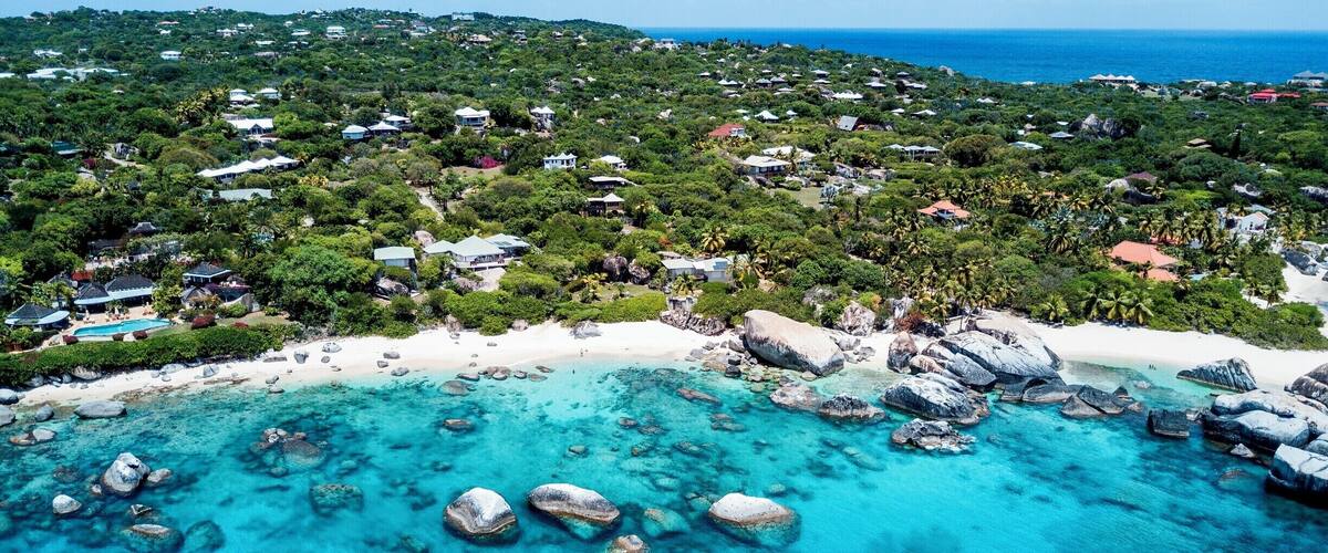A coastal area with clear turquoise waters, white sandy beaches, and scattered boulders.