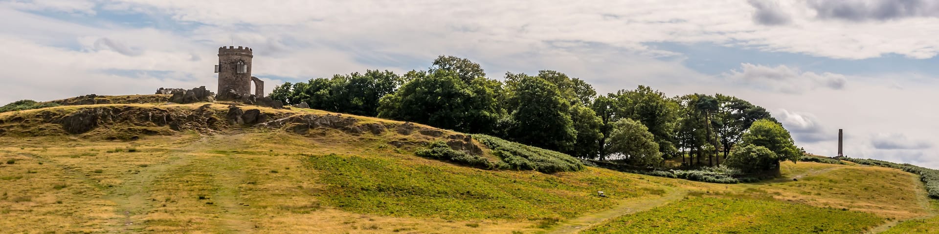 A grassy hill with a tower and trees.