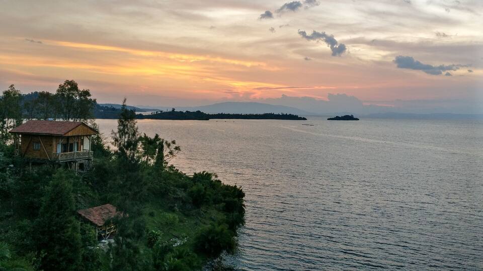 A wooden house on stilts by a calm sea with a sunset in the background.