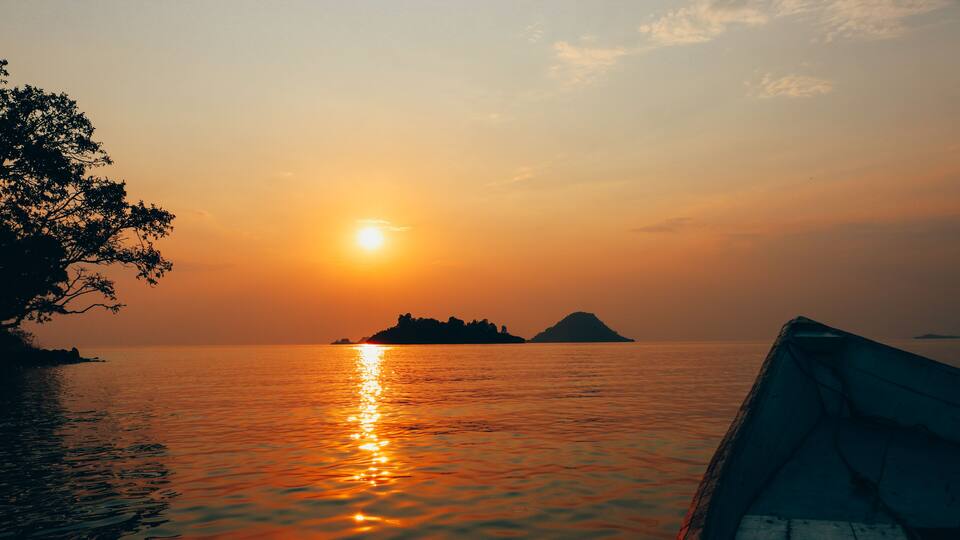 A sunset over calm waters with a boat docked on the left and an island in the distance.