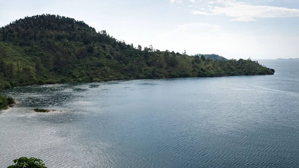 A calm lake surrounded by forested hills and distant mountains.