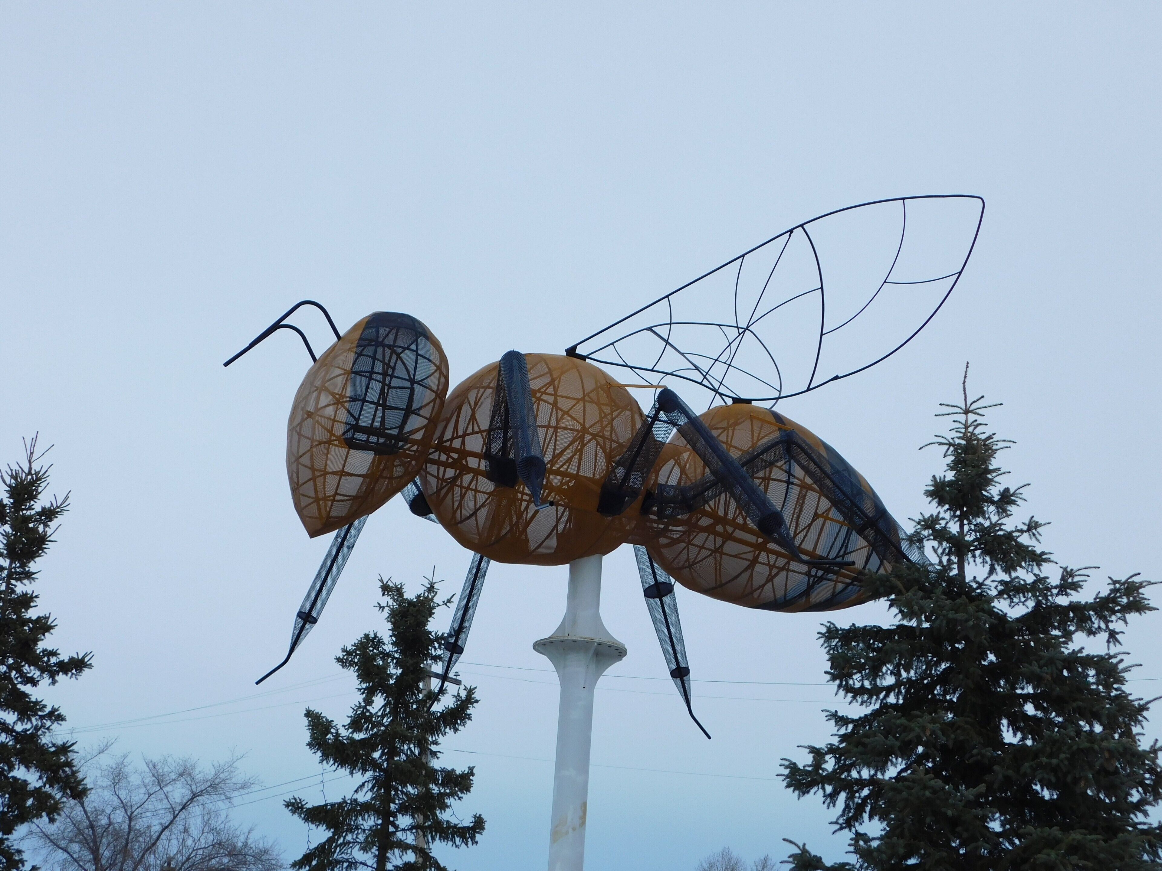 A large ant sculpture with wings, surrounded by trees.