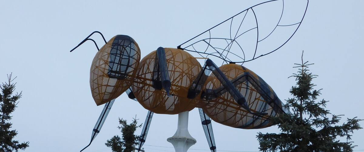 A large ant sculpture with wings, surrounded by trees.