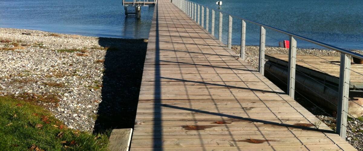 A wooden pier extending into calm waters, with a clear sky and distant mountains.