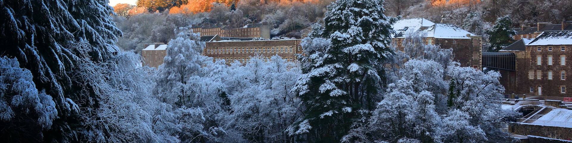 A snow-covered landscape with a river, trees, and buildings.