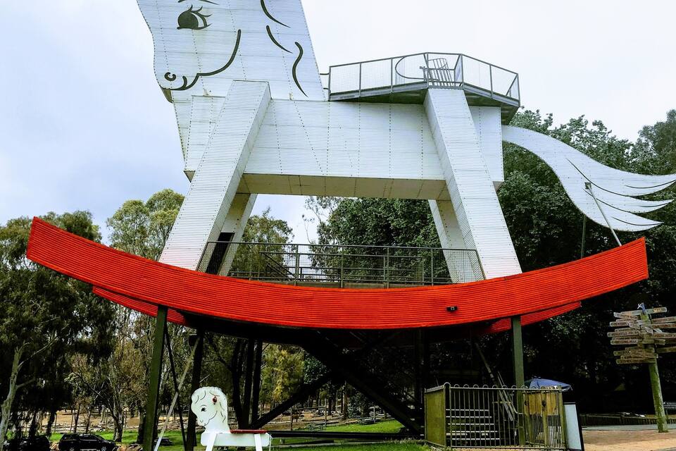 Un'ampia scultura bianca a forma di cavallo con una piattaforma rossa in un parco.