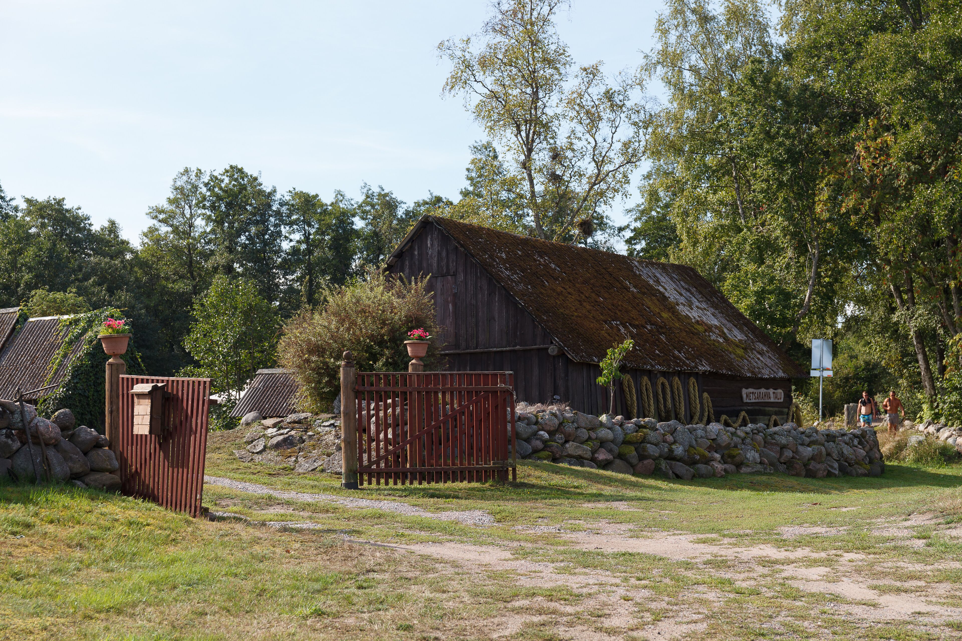 A rustic barn with a moss-covered roof, surrounded by a stone wall and lush greenery.
