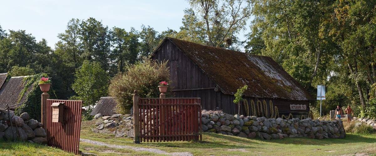 A rustic barn with a moss-covered roof, surrounded by a stone wall and lush greenery.