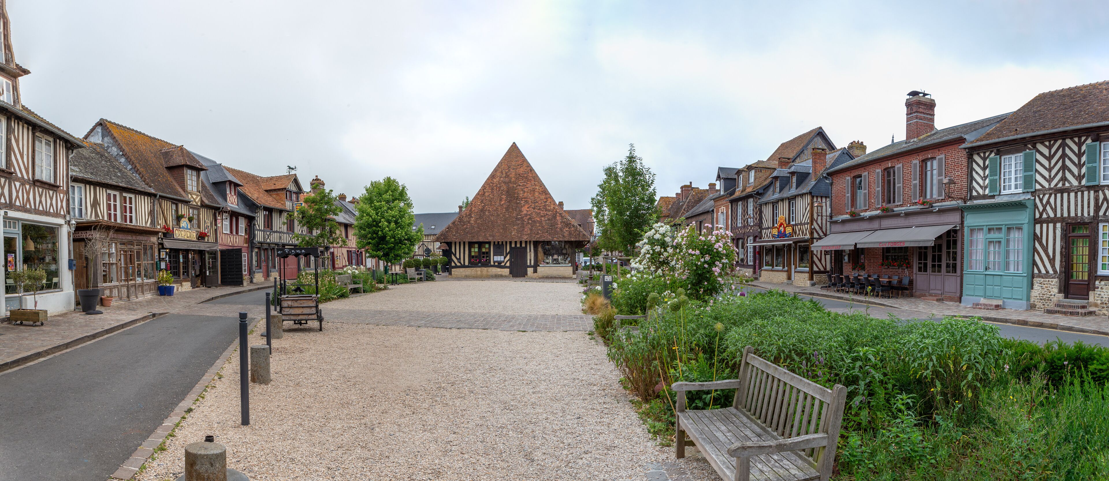 A cobblestone street with traditional half-timbered buildings, a thatched-roof structure, and benches.