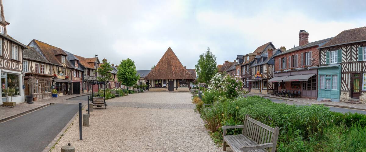 A cobblestone street with traditional half-timbered buildings, a thatched-roof structure, and benches.