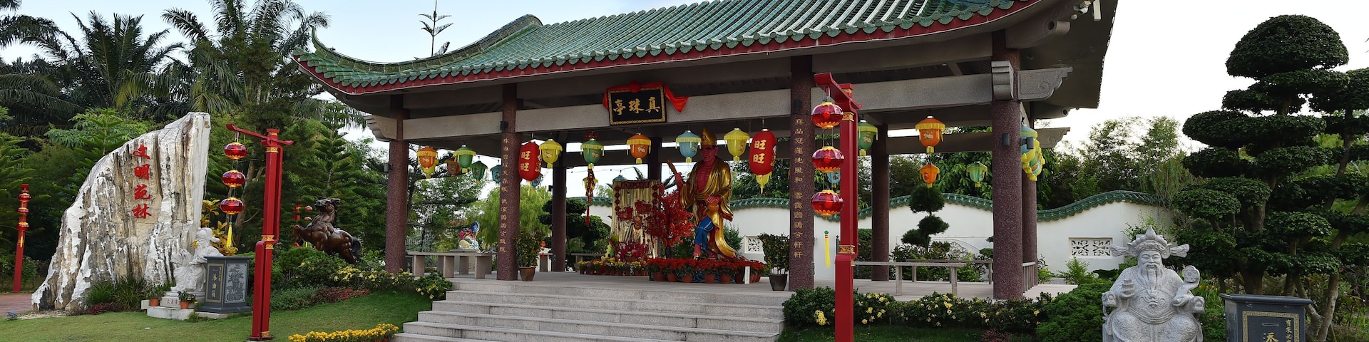 Um pavilhão chinês tradicional com telhado verde, rodeado por estátuas e lanternas vermelhas.