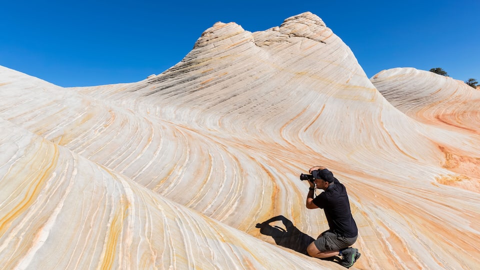 A photographer taking a photo of a large, wave-like rock formation with a clear blue sky in the background.