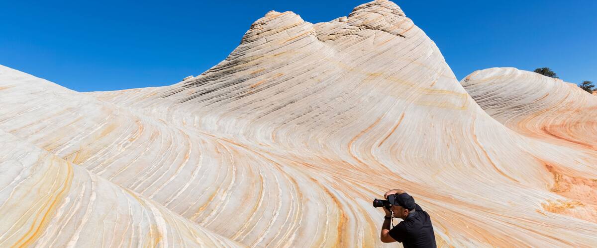 A photographer taking a photo of a large, wave-like rock formation with a clear blue sky in the background.