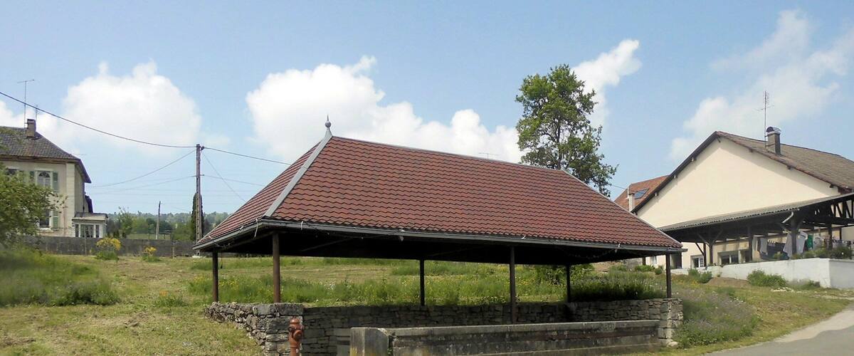A rural scene with a covered pavilion, stone walls, a road, and houses.