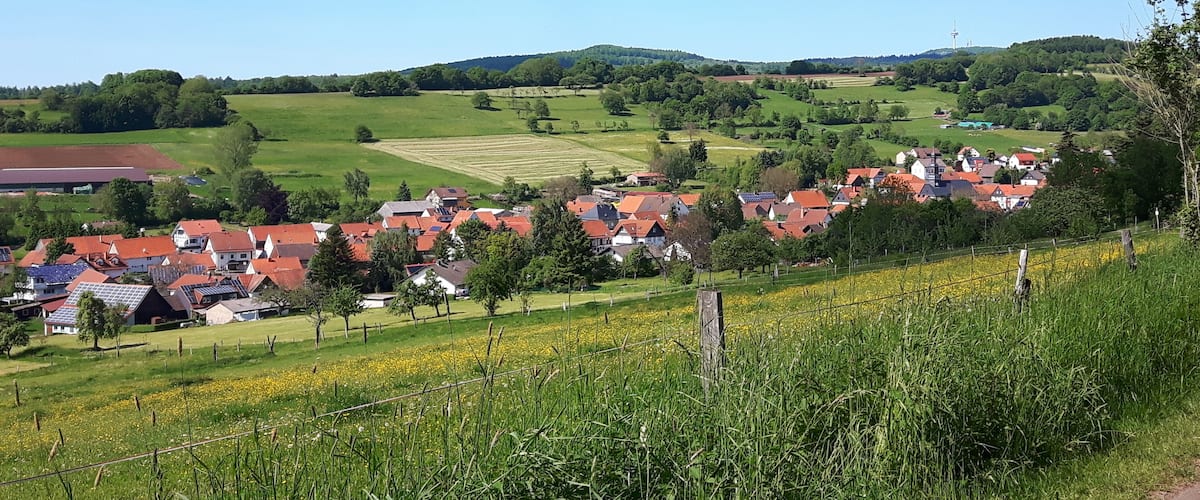 A rural village with red-roofed houses, green fields, and a clear blue sky.