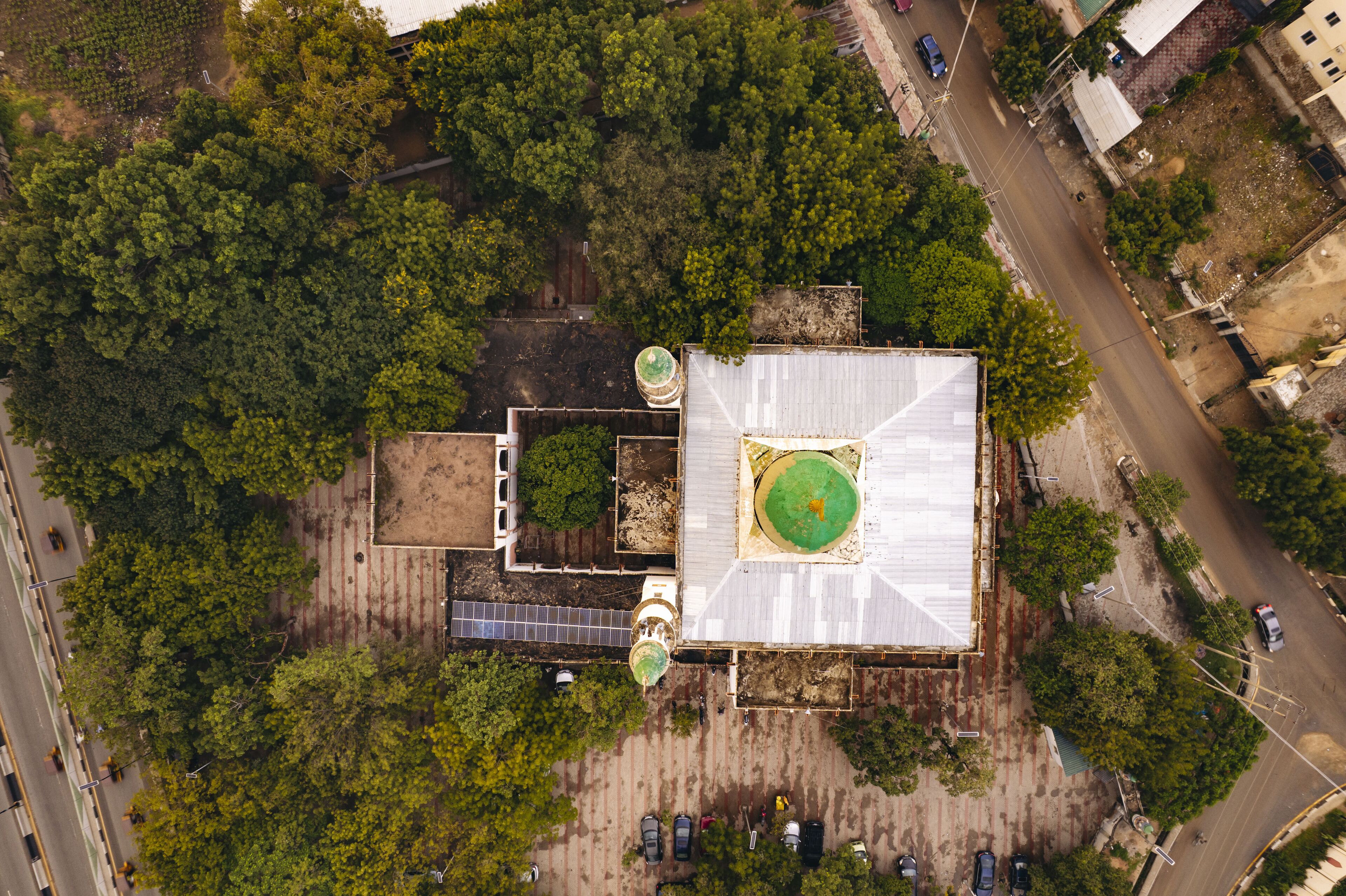 Aerial view of a mosque with a vibrant green dome nestled amidst dense trees and adjacent to a road, Zaria Road, Kano, Kano, Nigeria.