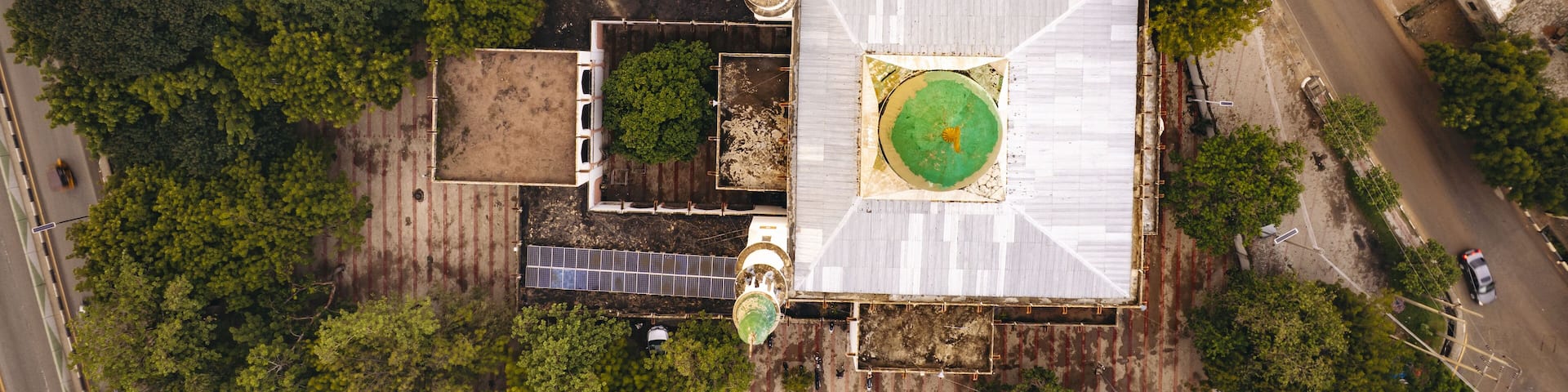 Aerial view of a mosque with a vibrant green dome nestled amidst dense trees and adjacent to a road, Zaria Road, Kano, Kano, Nigeria.