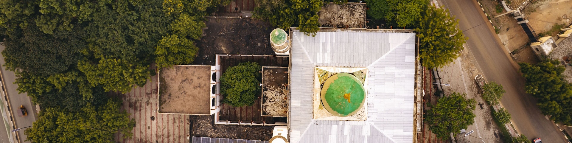 Aerial view of a mosque with a vibrant green dome nestled amidst dense trees and adjacent to a road, Zaria Road, Kano, Kano, Nigeria.