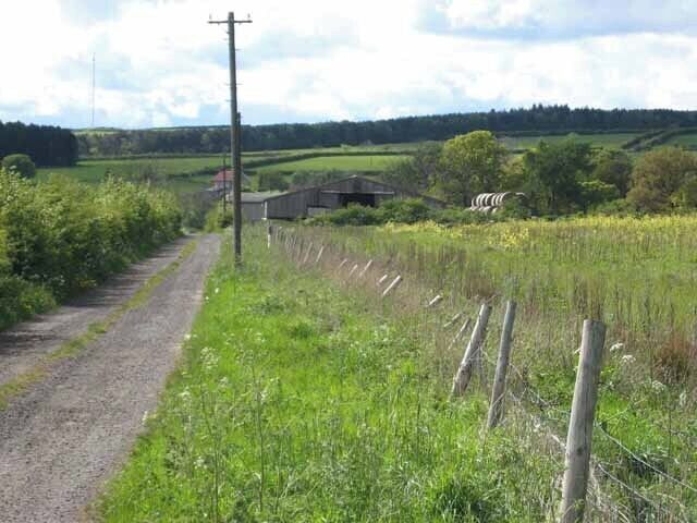 A rural road with a fence and a building in the distance.