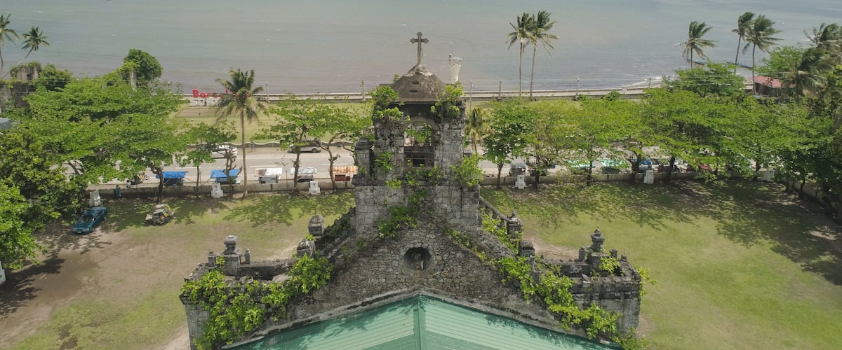A coastal view with a historic church, palm trees, and a beach.