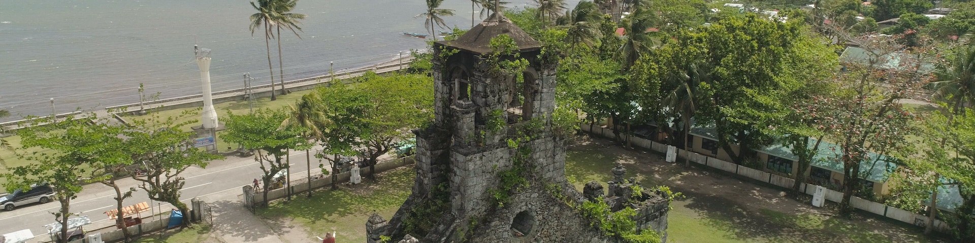 Paisaje costero con una torre desgastada, palmeras y vista al océano.