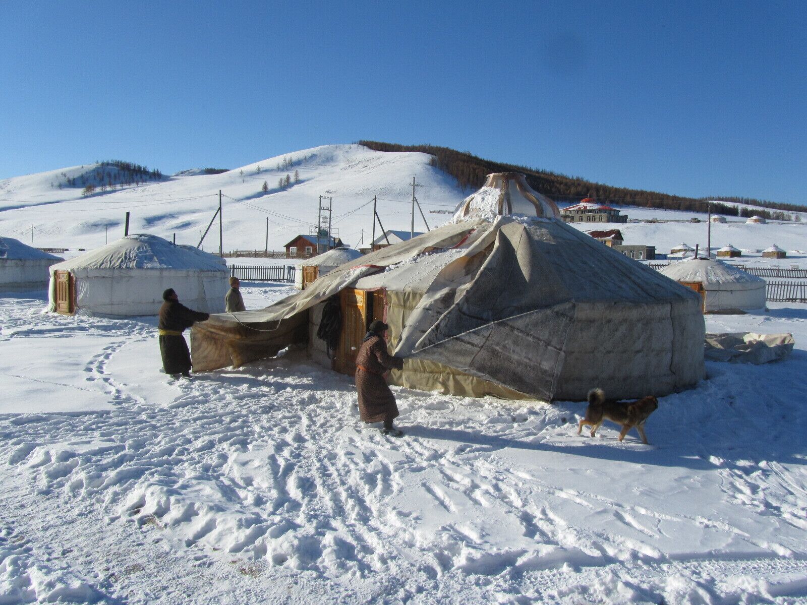 A snowy landscape with yurts and a person handling a tarp.