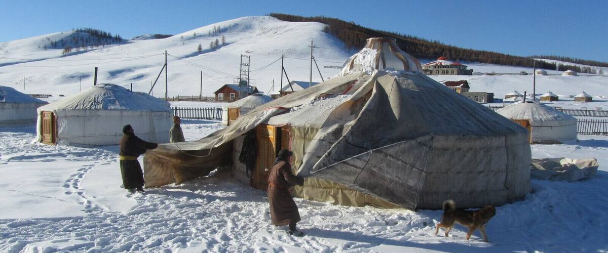 A snowy landscape with yurts and a person handling a tarp.