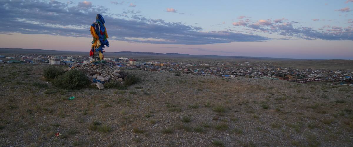A statue on a hill overlooking a town with a clear sky and distant mountains.