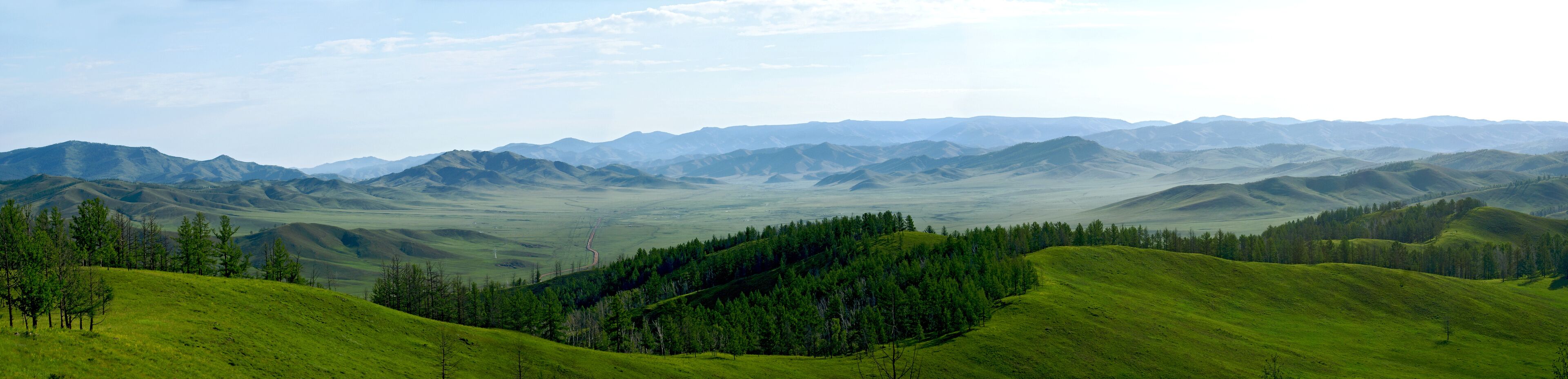 Rolling green hills, distant mountains, and scattered trees.