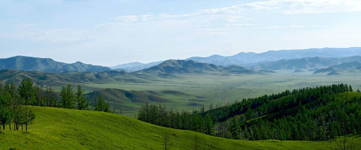 Rolling green hills, distant mountains, and scattered trees.
