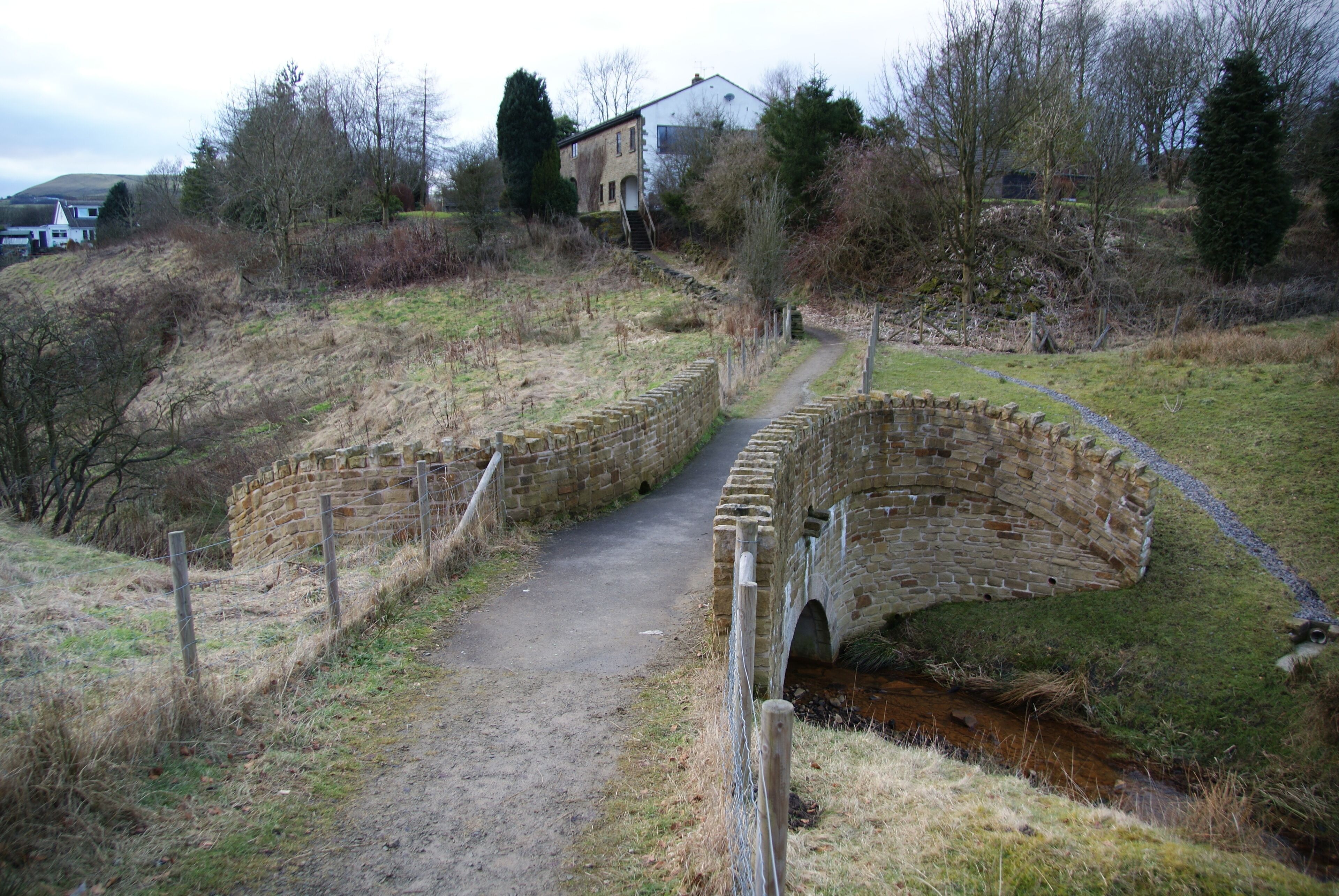 A stone bridge over a narrow stream, surrounded by grassy terrain and trees.