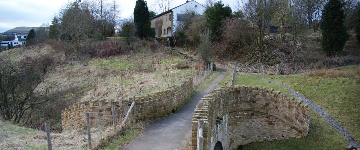 A stone bridge over a narrow stream, surrounded by grassy terrain and trees.