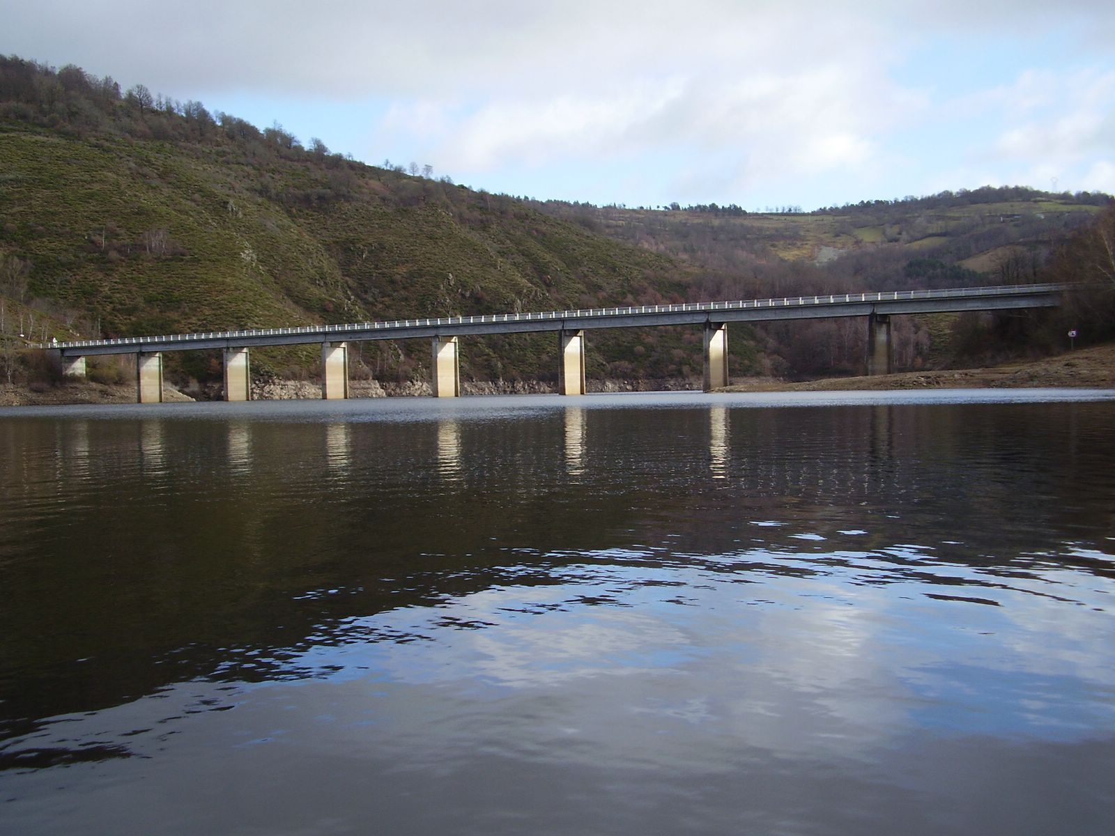 A bridge over a calm river with hills in the background.