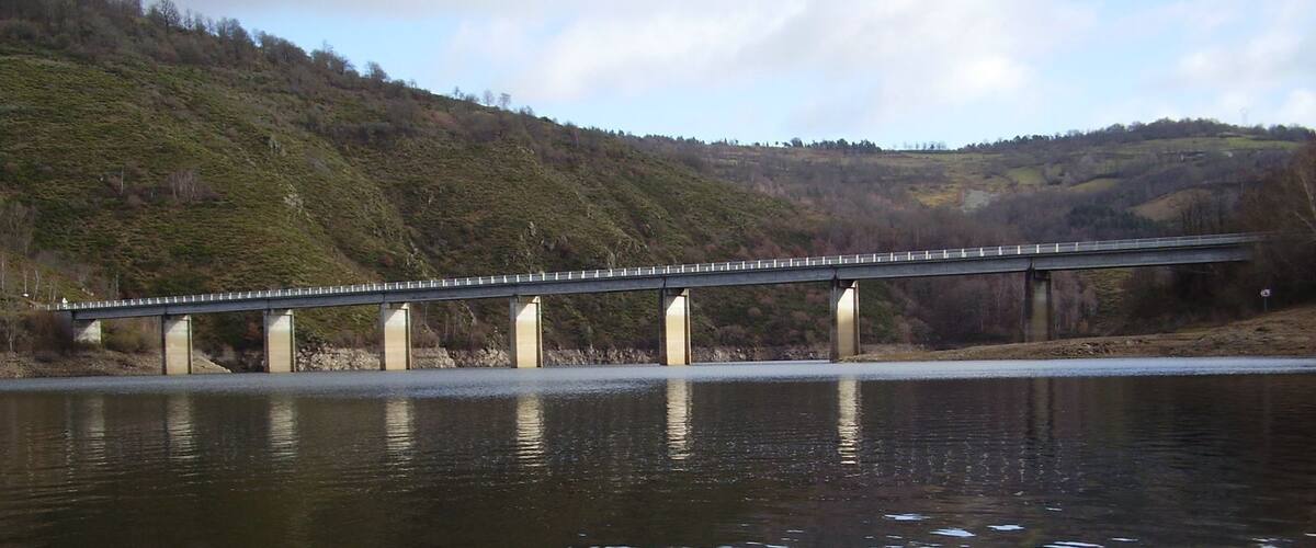 A bridge over a calm river with hills in the background.