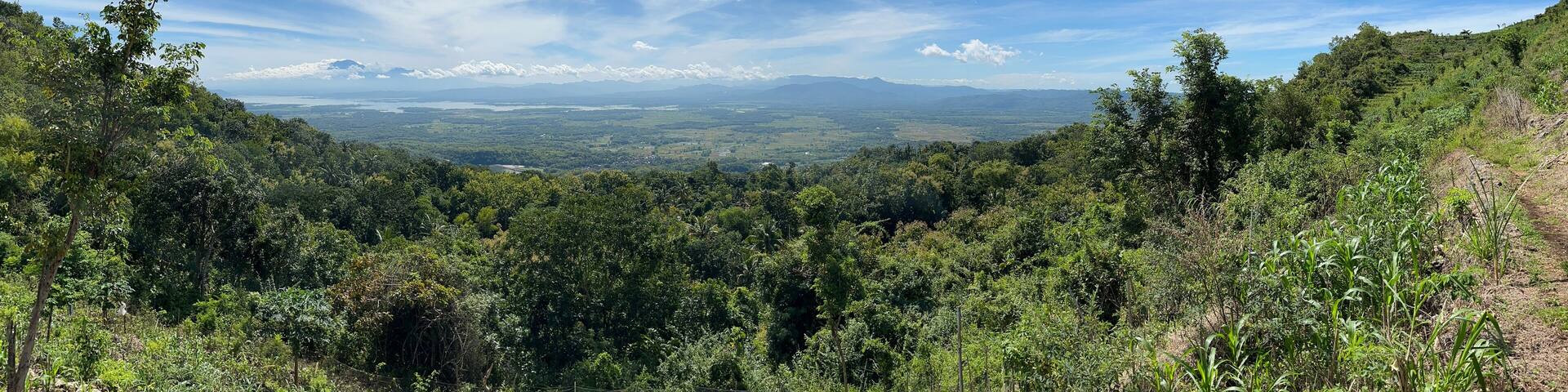 Stunning aerial view of a lush tropical valley in southern Wonogiri, Indonesia, with green fields, lakes, rural villages, and distant mountains under a bright blue sky. footage taken from Pokoh Hill.
