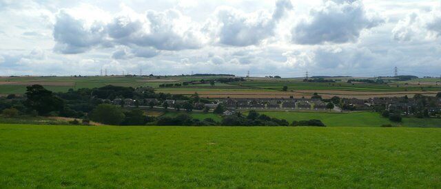 A rural landscape with fields, a village, and distant power lines.