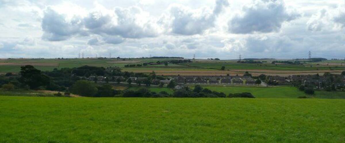 A rural landscape with fields, a village, and distant power lines.