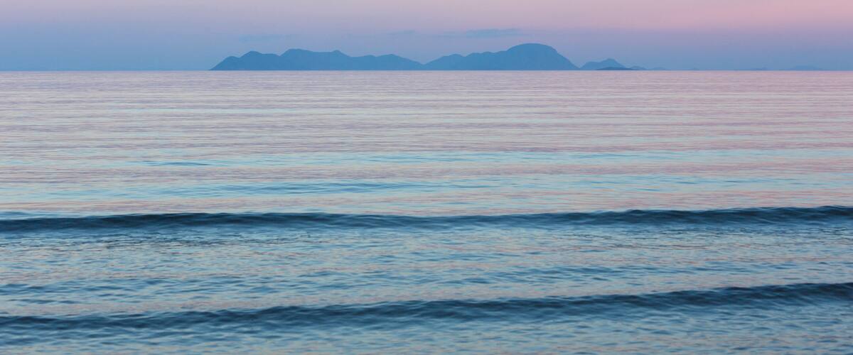 A calm sea with gentle waves and distant mountains under a pastel sky.