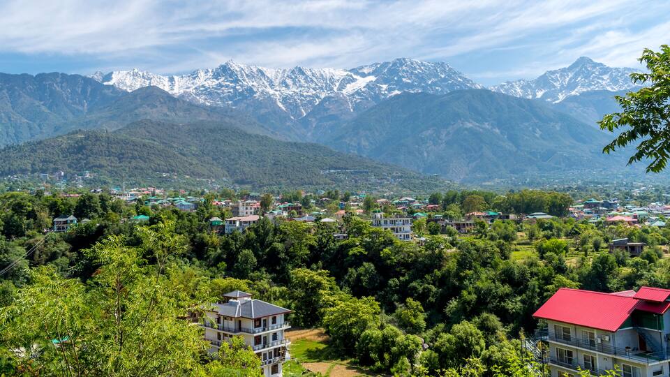 A mountainous landscape with snow-capped peaks in the background, a town with colorful houses in the foreground, and lush green vegetation.