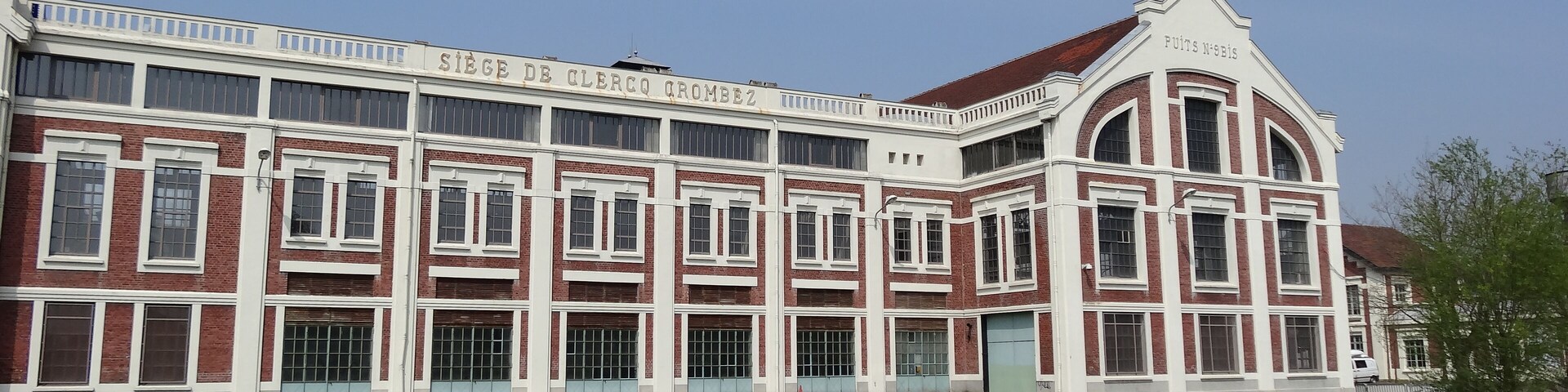 A large, historic building with red brick and white trim, featuring multiple windows and a prominent arched entrance.