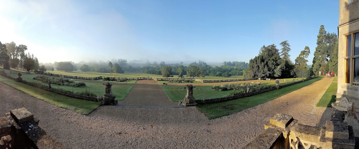 A historic estate with a formal garden, a statue, and a large building with a balcony.