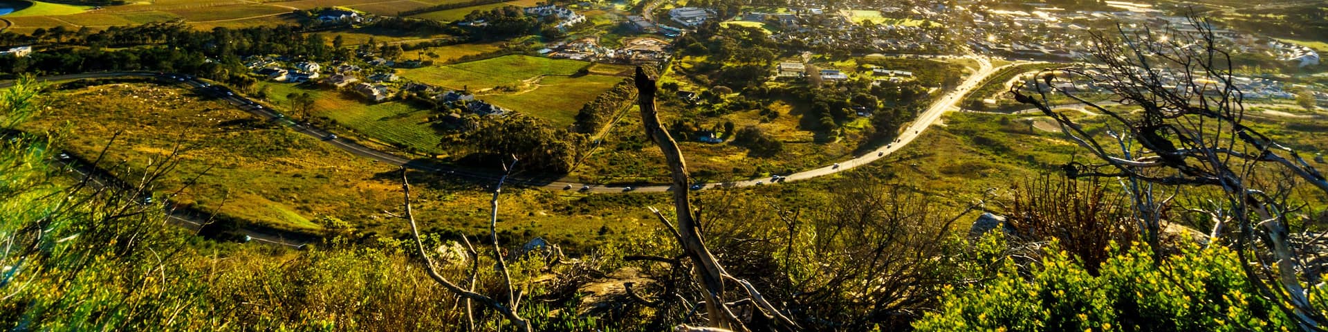 A panoramic view of a valley with mountains in the background, a winding road, and a clear sky.