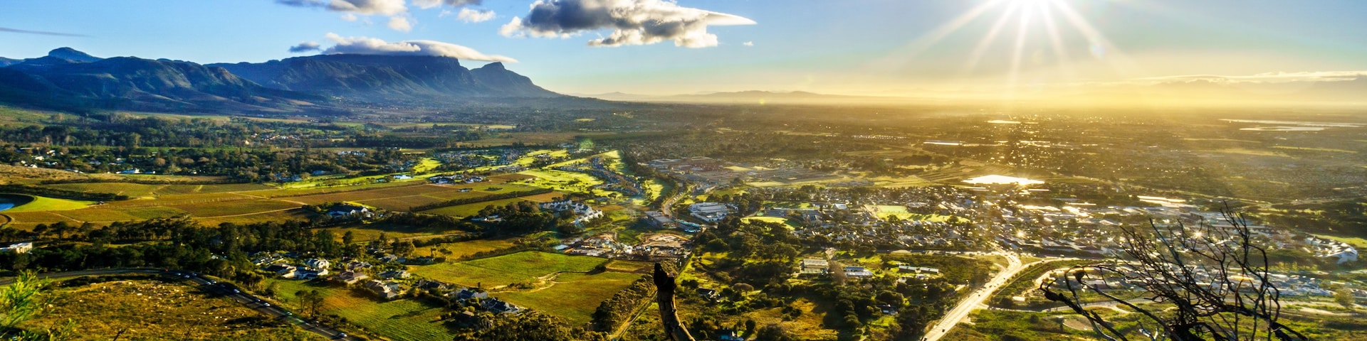 Vista panorâmica de um vale com montanhas ao fundo, uma estrada sinuosa e céu claro.