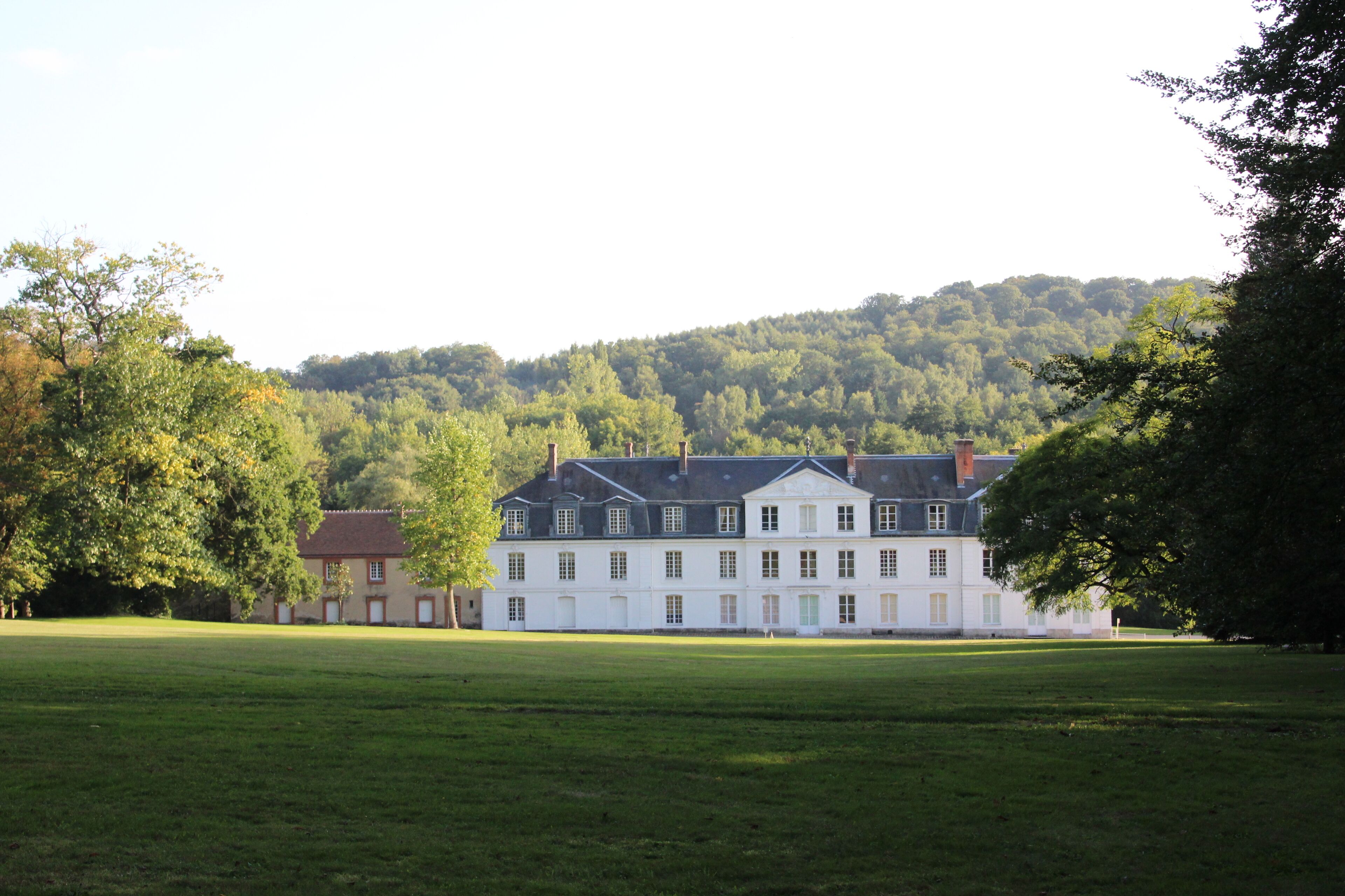 A large white building with a symmetrical facade, surrounded by a well-maintained lawn and trees.